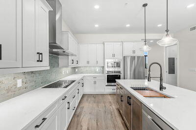 kitchen with sink, white cabinetry, hanging light fixtures, appliances with stainless steel finishes, and wall chimney range hood