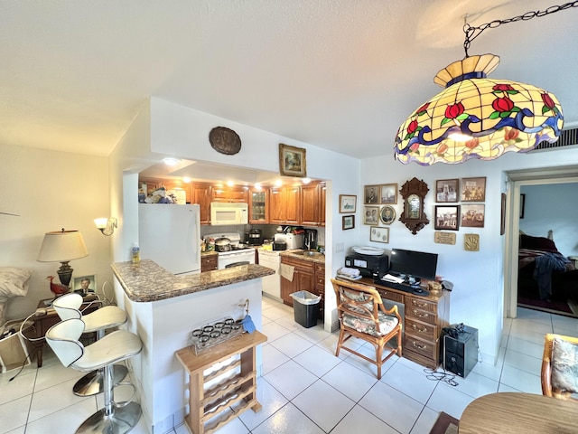 kitchen featuring a kitchen bar, dark stone countertops, light tile patterned floors, kitchen peninsula, and white appliances