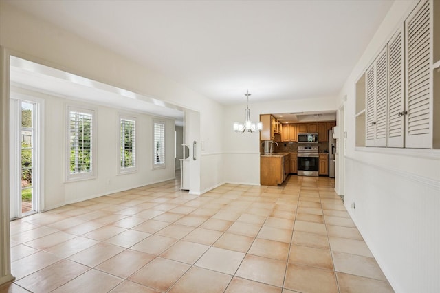 interior space with sink, appliances with stainless steel finishes, backsplash, a notable chandelier, and light tile patterned flooring