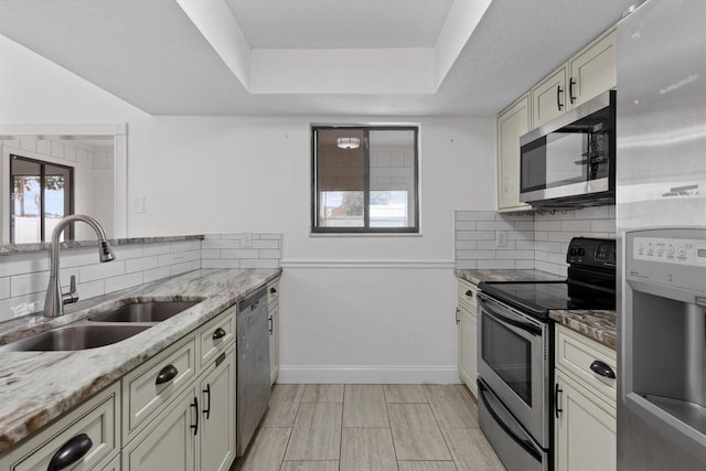 kitchen featuring appliances with stainless steel finishes, sink, backsplash, light stone counters, and cream cabinetry