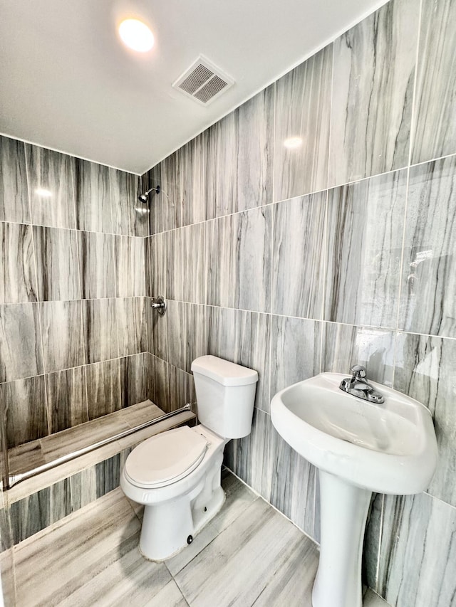 bathroom with a tile shower, tile walls, and toilet