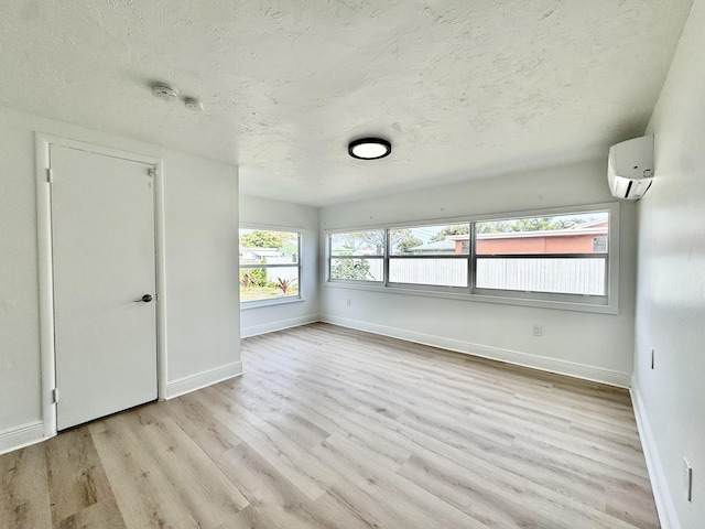 empty room featuring a wall mounted air conditioner, light hardwood / wood-style flooring, and a textured ceiling