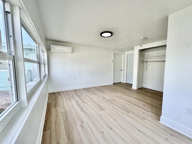 unfurnished bedroom with an AC wall unit, two closets, and light hardwood / wood-style flooring