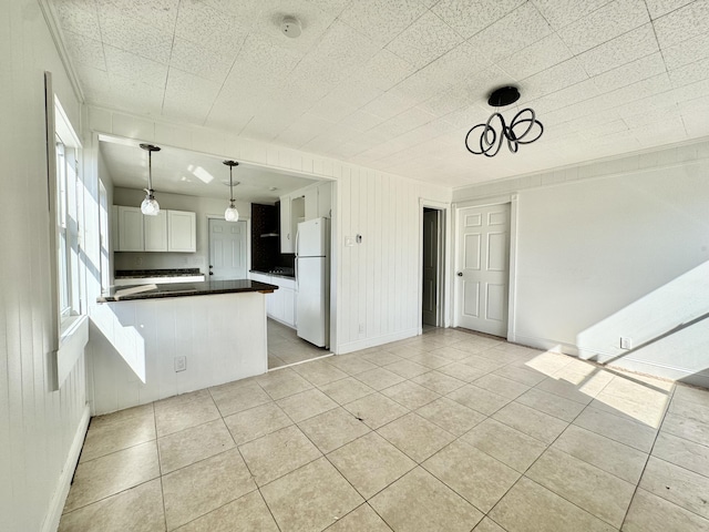 kitchen featuring light tile patterned flooring, decorative light fixtures, kitchen peninsula, white fridge, and white cabinets