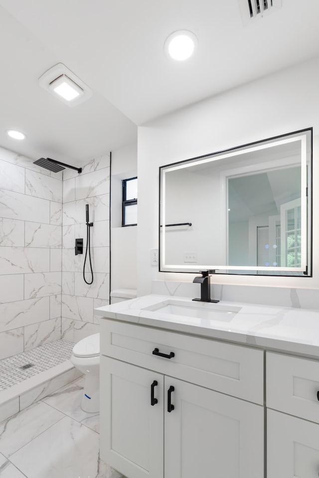 bathroom featuring vanity, a tile shower, and toilet