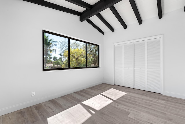 unfurnished bedroom with lofted ceiling with beams, a closet, and light hardwood / wood-style flooring