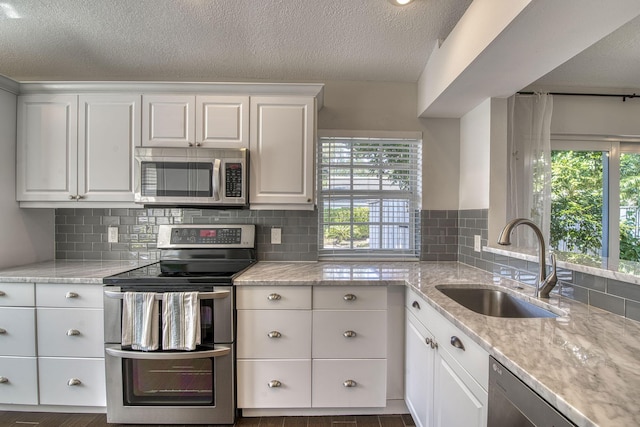kitchen featuring appliances with stainless steel finishes, a sink, plenty of natural light, backsplash, and a textured ceiling
