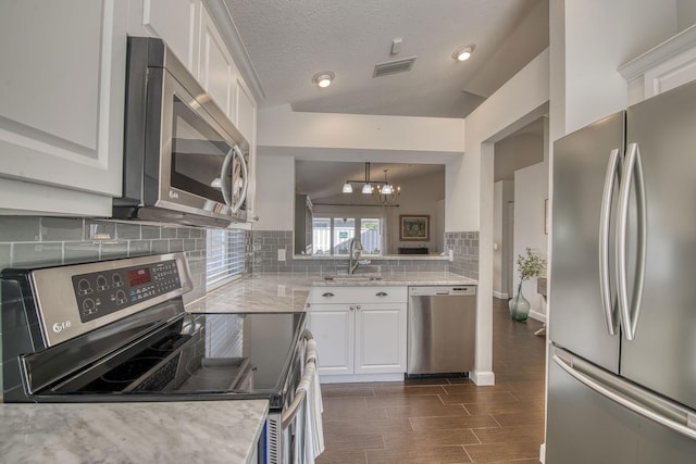 kitchen featuring appliances with stainless steel finishes, a sink, decorative backsplash, white cabinets, and a chandelier