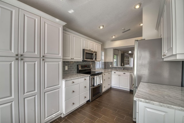 kitchen with stainless steel appliances, tasteful backsplash, lofted ceiling, and white cabinets