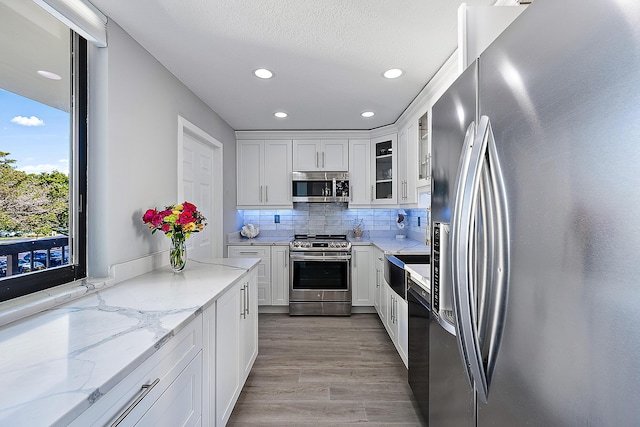 kitchen with light hardwood / wood-style flooring, white cabinetry, stainless steel appliances, tasteful backsplash, and light stone countertops