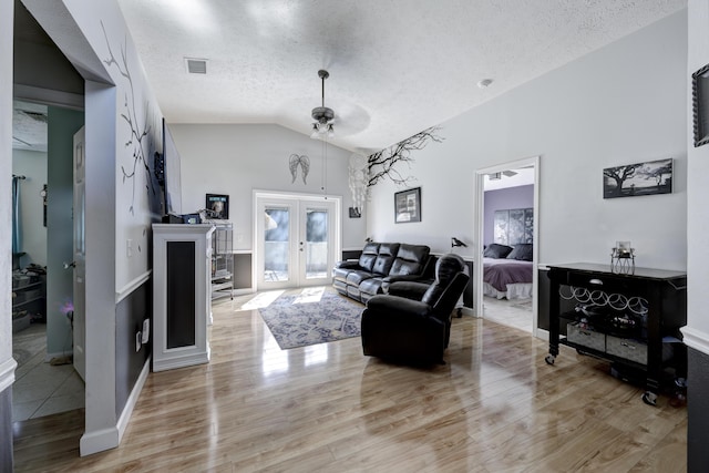 living room with french doors, lofted ceiling, light hardwood / wood-style floors, and a textured ceiling