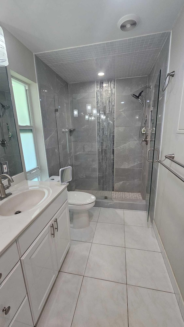 bathroom with a shower with door, vanity, tile patterned floors, and toilet