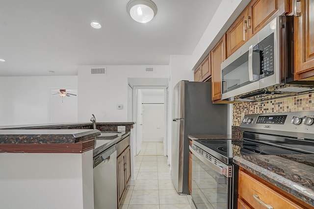 kitchen featuring light tile patterned flooring, sink, appliances with stainless steel finishes, dark stone counters, and backsplash