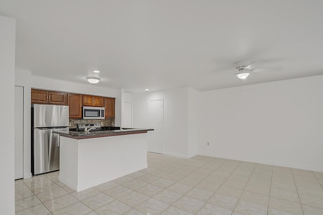 kitchen featuring ceiling fan, a center island with sink, stainless steel appliances, light tile patterned flooring, and decorative backsplash