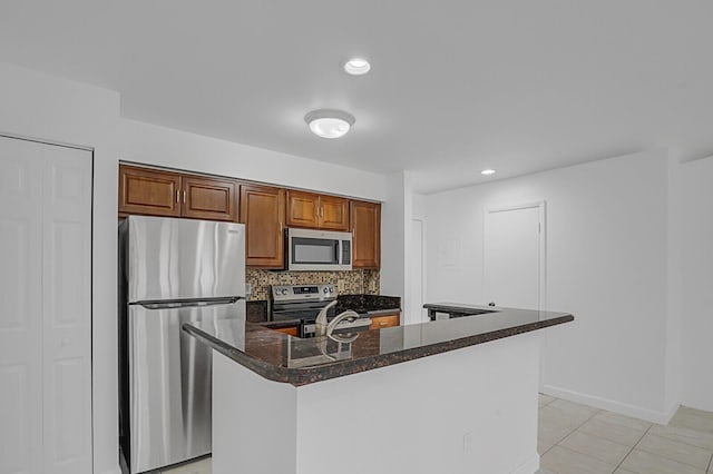 kitchen with light tile patterned flooring, tasteful backsplash, dark stone counters, an island with sink, and stainless steel appliances