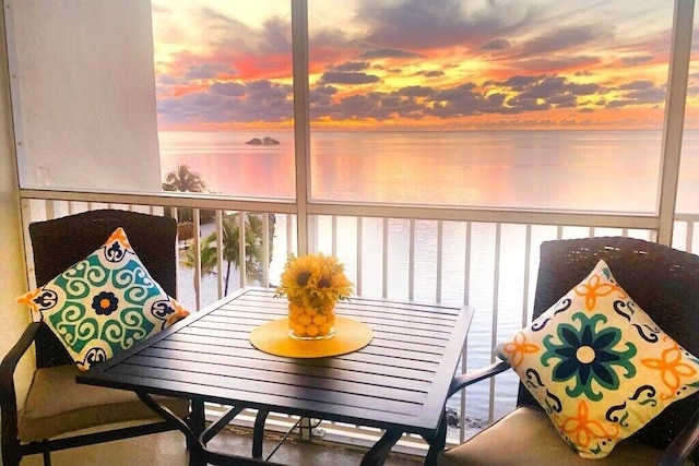 balcony at dusk featuring a water view