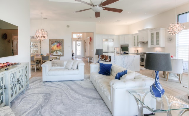 living room featuring a towering ceiling, ceiling fan with notable chandelier, and light hardwood / wood-style flooring