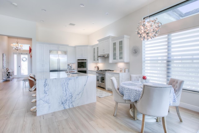 kitchen featuring high end appliances, a notable chandelier, decorative light fixtures, and white cabinets