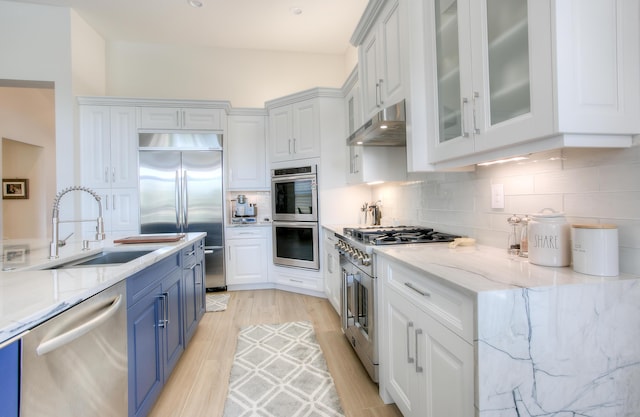 kitchen featuring tasteful backsplash, sink, high end appliances, light stone countertops, and blue cabinetry