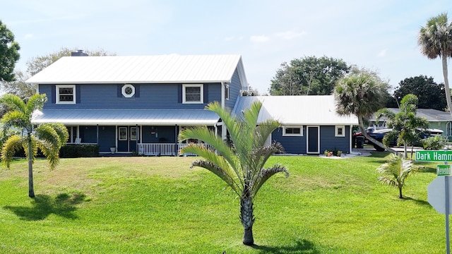 view of front facade with a front yard, covered porch, metal roof, and a chimney