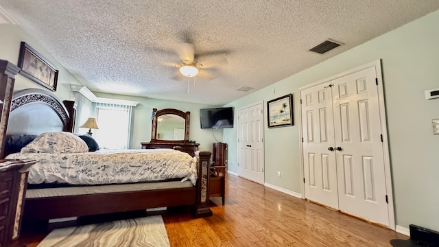 bedroom with baseboards, visible vents, a ceiling fan, wood finished floors, and multiple closets