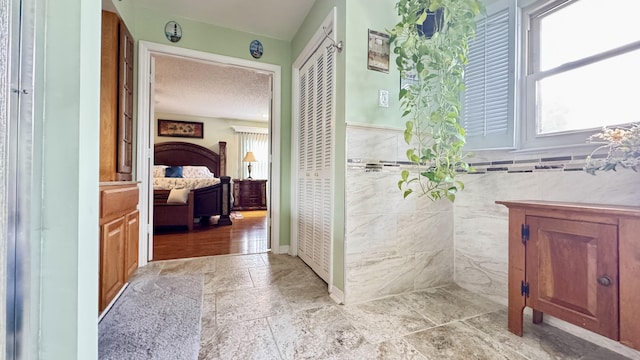 ensuite bathroom featuring stone tile floors, connected bathroom, a wainscoted wall, a textured ceiling, and tile walls