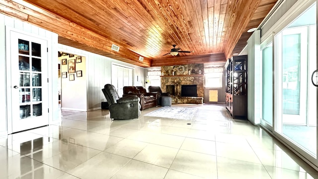 tiled living room with ceiling fan, a stone fireplace, visible vents, and wood ceiling