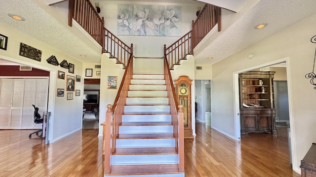 stairs featuring a textured ceiling, a towering ceiling, baseboards, and hardwood / wood-style flooring