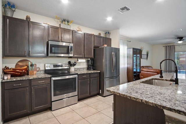 kitchen with sink, light tile patterned floors, dark brown cabinets, stainless steel appliances, and light stone countertops