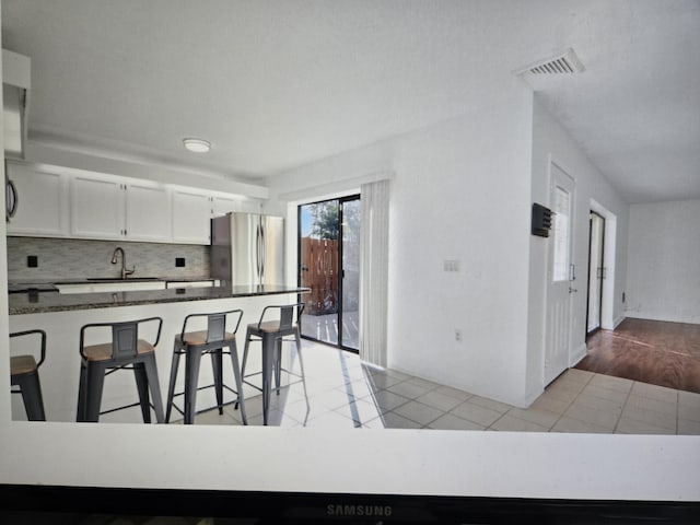 kitchen with sink, stainless steel fridge, white cabinetry, backsplash, and a kitchen bar