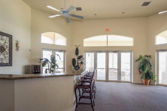 kitchen featuring french doors, ceiling fan, a kitchen breakfast bar, carpet floors, and a towering ceiling