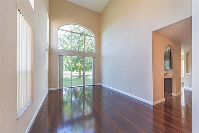 spare room with a healthy amount of sunlight, dark hardwood / wood-style flooring, and high vaulted ceiling