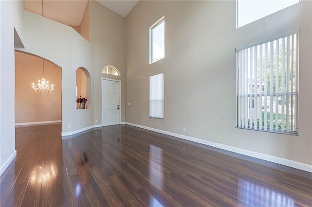 empty room with an inviting chandelier, dark hardwood / wood-style floors, and a high ceiling