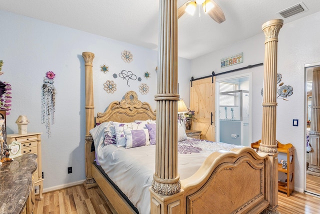 bedroom with ornate columns, ceiling fan, a barn door, and light hardwood / wood-style floors