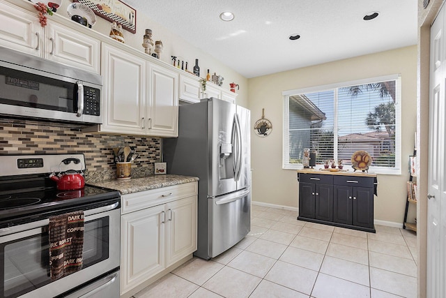 kitchen featuring appliances with stainless steel finishes, tasteful backsplash, white cabinetry, light tile patterned floors, and light stone countertops