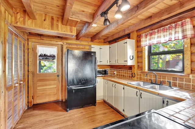 kitchen featuring black refrigerator, white cabinetry, sink, tile counters, and wood ceiling