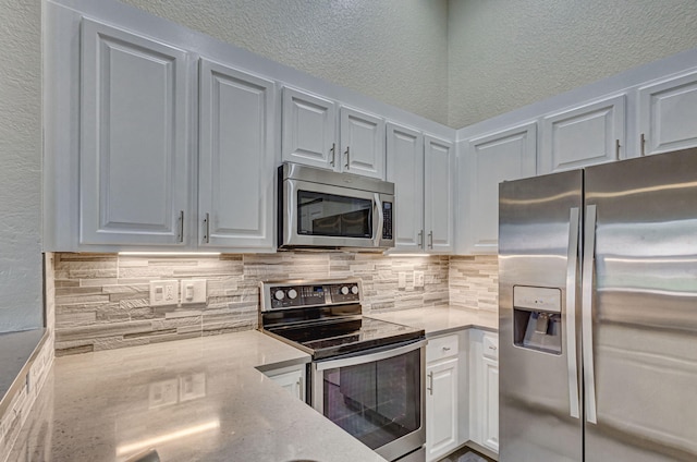 kitchen with appliances with stainless steel finishes, white cabinets, light stone counters, and decorative backsplash