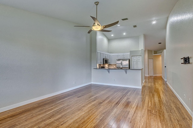 unfurnished living room featuring a towering ceiling, ceiling fan, and light hardwood / wood-style flooring