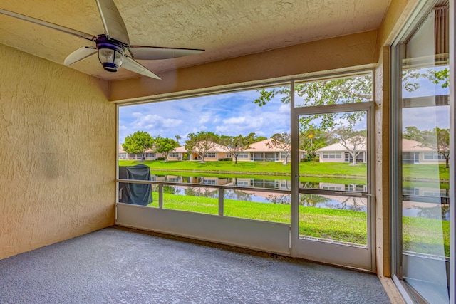 unfurnished sunroom featuring ceiling fan and a water view