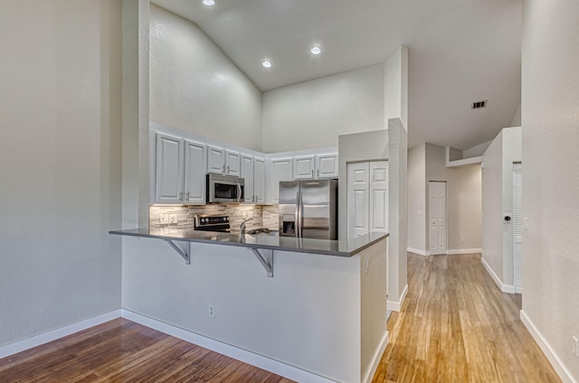 kitchen with a breakfast bar, white cabinetry, kitchen peninsula, stainless steel appliances, and decorative backsplash