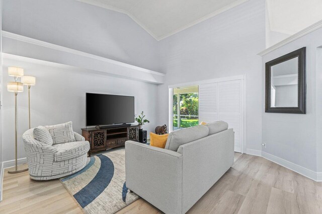 living room with crown molding, a towering ceiling, and light wood-type flooring