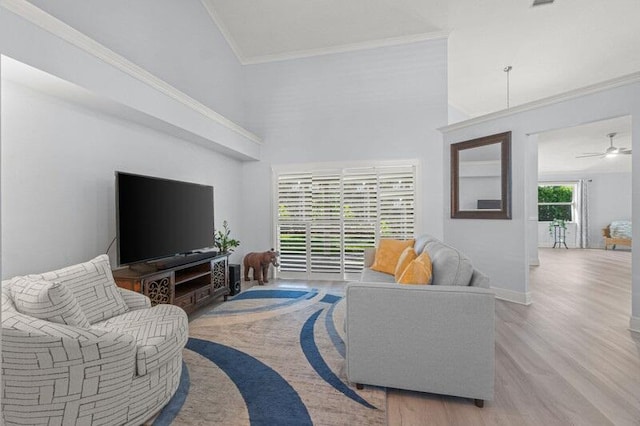 living room with ceiling fan, crown molding, a high ceiling, and light wood-type flooring