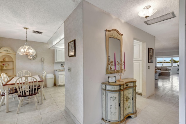 corridor featuring an inviting chandelier, light tile patterned floors, and a textured ceiling