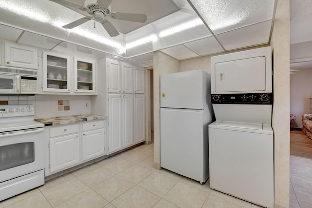 kitchen featuring white appliances, stacked washing maching and dryer, light tile patterned floors, and white cabinets