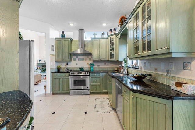 kitchen featuring green cabinets, stainless steel appliances, sink, and wall chimney range hood