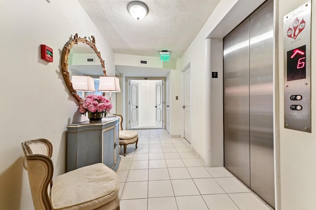 hall with elevator, a textured ceiling, and light tile patterned floors