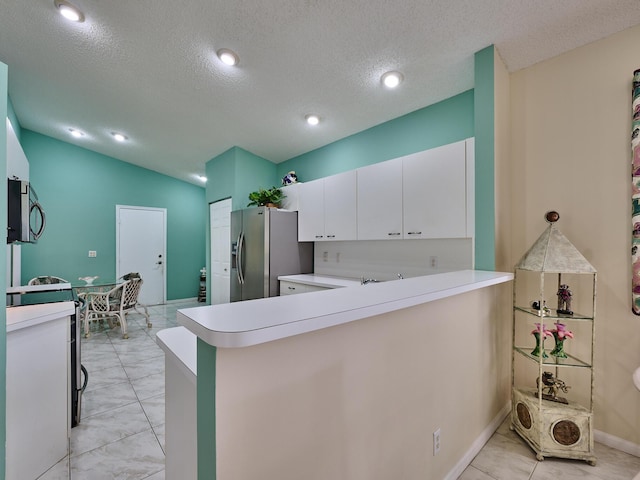 kitchen featuring lofted ceiling, appliances with stainless steel finishes, a textured ceiling, white cabinets, and kitchen peninsula