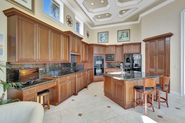 kitchen featuring a center island with sink, dark stone countertops, ornamental molding, a towering ceiling, and black appliances