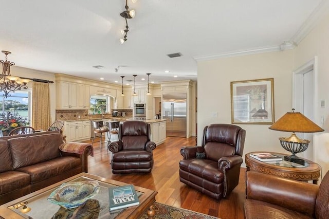 living area featuring light wood finished floors, ornamental molding, visible vents, and a notable chandelier