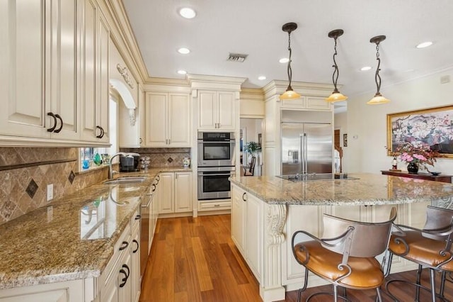 kitchen featuring visible vents, a center island, stainless steel appliances, a kitchen bar, and a sink